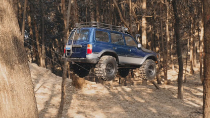 FMS FCX10 PRO Toyota LC80 RS V2 brushless crawler articulating on a forest obstacle